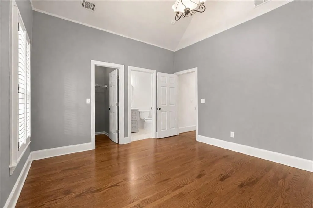 Unfurnished bedroom featuring a spacious closet, lofted ceiling, dark wood-type flooring, and connected bathroom