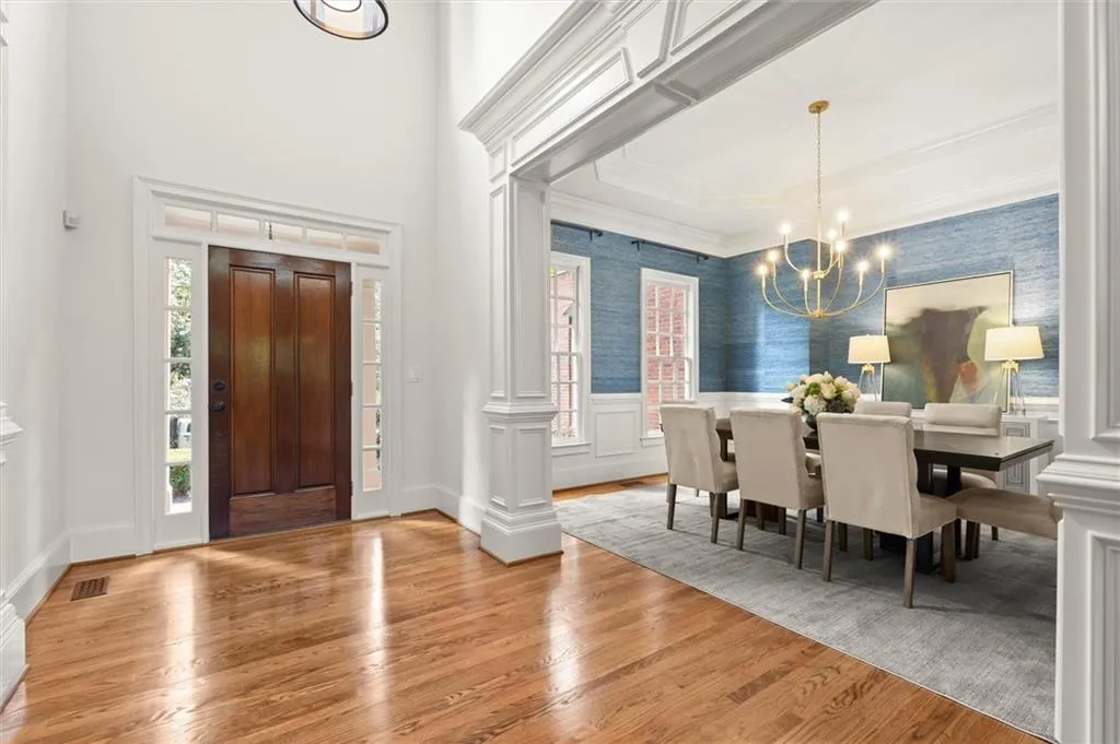 Entryway with wallpapered walls, light wood-type flooring, a chandelier, wainscoting, and a high ceiling