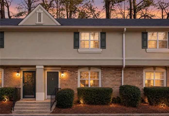 Brick and stucco exterior with dark shutters, dual entryways, and exterior lighting