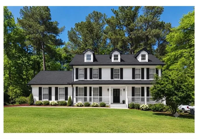 White exterior with black shutters, dormer windows, a full-width front porch, and a lush green lawn