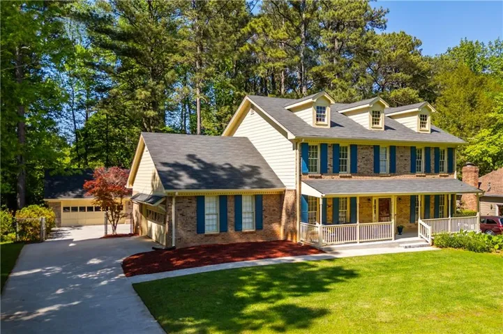 Brick and siding exterior featuring a covered front porch, multiple dormer windows, a two-car garage, and a separate detached garage structure
