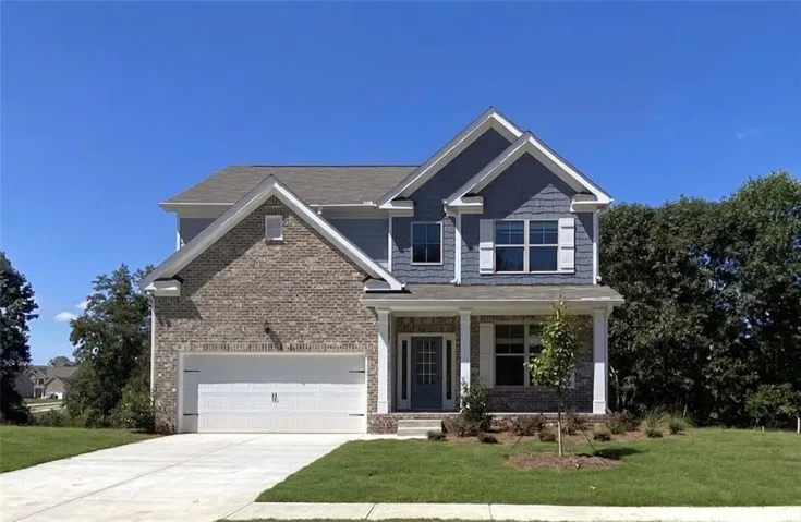 Two-story residence featuring a brick and siding exterior with decorative gables, an attached two-car garage, a covered front porch with column supports, and a paved driveway