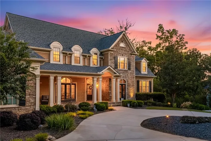 View of front of house with stone siding, roof with shingles, a porch, and curved driveway