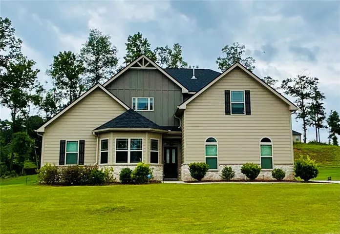 Expansive front lawn, two-story residence with a gabled roof, mixed siding exterior, stone accents, and a prominent bay window