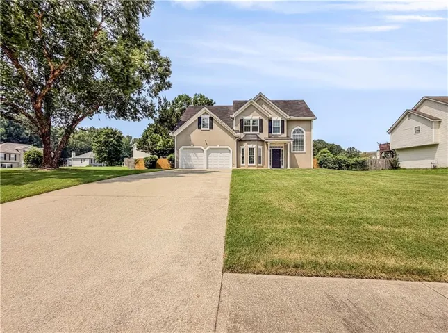 Two-story residence featuring a two-car garage, bay windows, and arched windows, complemented by a concrete driveway and mature tree
