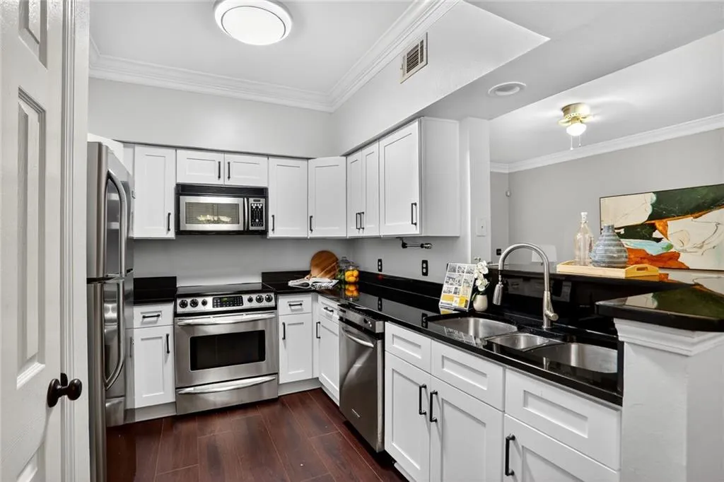 Kitchen featuring ornamental molding, dark countertops, dark wood-style flooring, stainless steel appliances, and white cabinetry