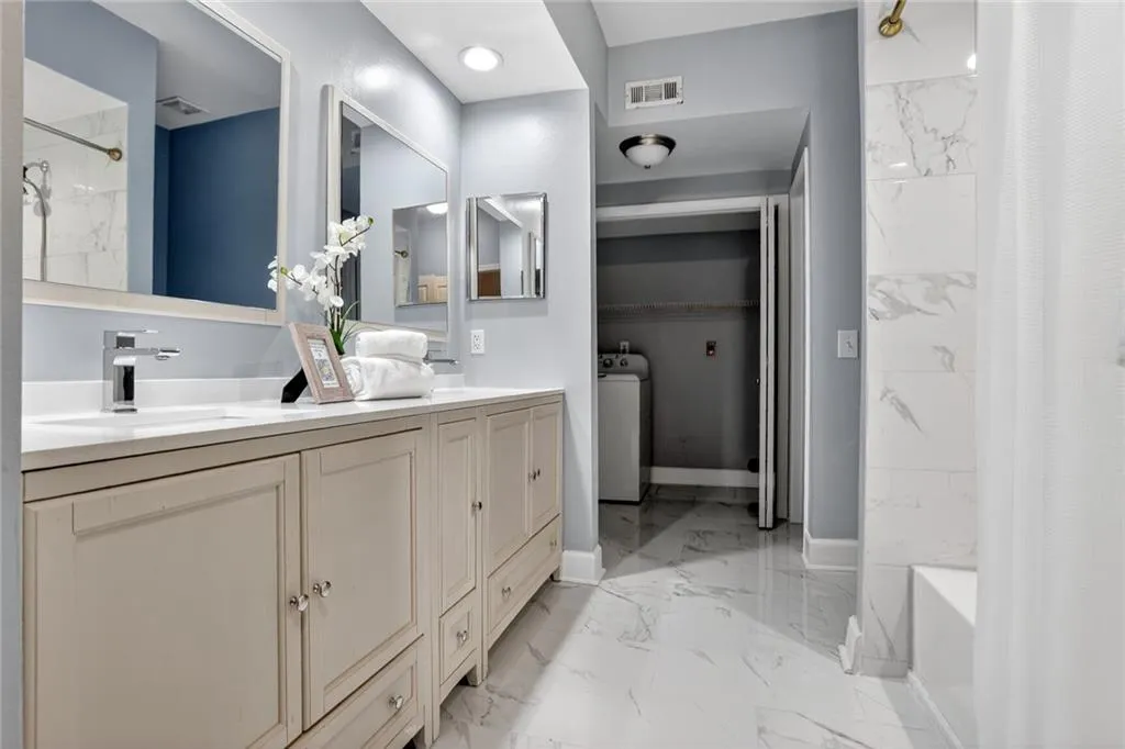 Bathroom with marble look tiles, double vanity, shower / bath combo, and washer / dryer
