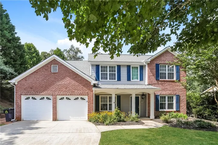 Brick and siding exterior featuring a two-car garage with arched window inserts, a covered front porch, blue window shutters, and a concrete driveway