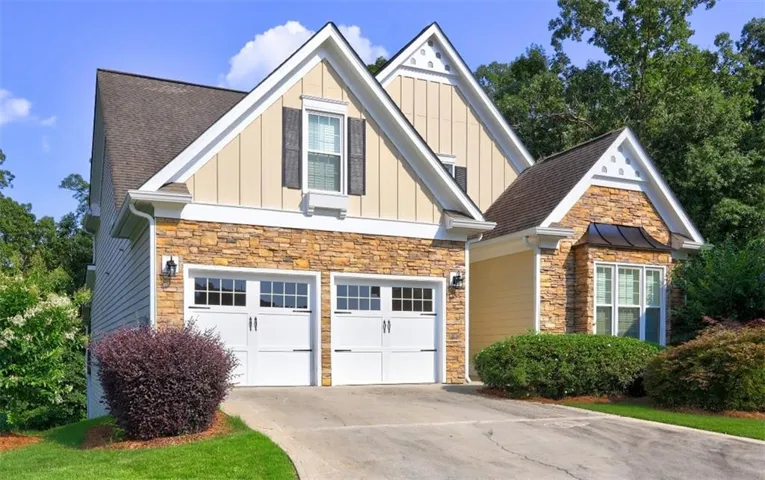 Stone and siding exterior featuring a two-car garage with carriage-style doors, a bay window, and a gabled roofline
