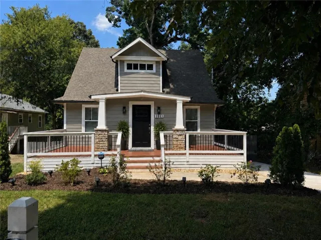 Siding exterior with dormer window, covered porch with stone columns, dark wood-finish porch flooring, black metal railings, and integrated landscaping