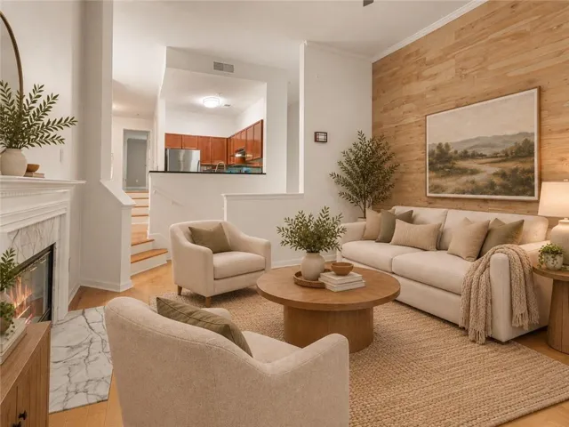 Hardwood flooring throughout, wood-paneled accent wall, and a fireplace with a white mantel and marble surround