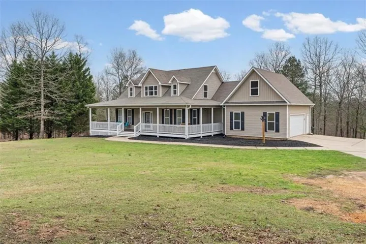 Gabled roofline, wrap-around porch, dormer windows, attached garage, and a concrete driveway
