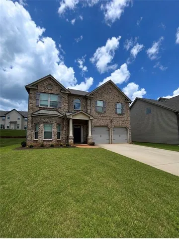 Brick facade with a two-car garage, manicured lawn, and concrete driveway