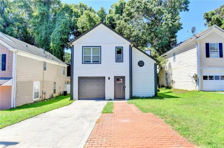 White exterior with dark trim accents, featuring a single-car garage and a red brick paver walkway