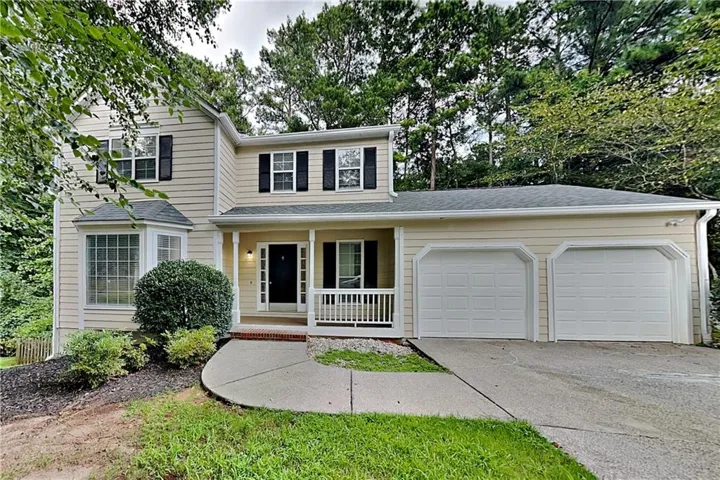 Two-story residence featuring light-toned siding, a covered front entry with white railings, a bay window, and an attached two-car garage with individual doors