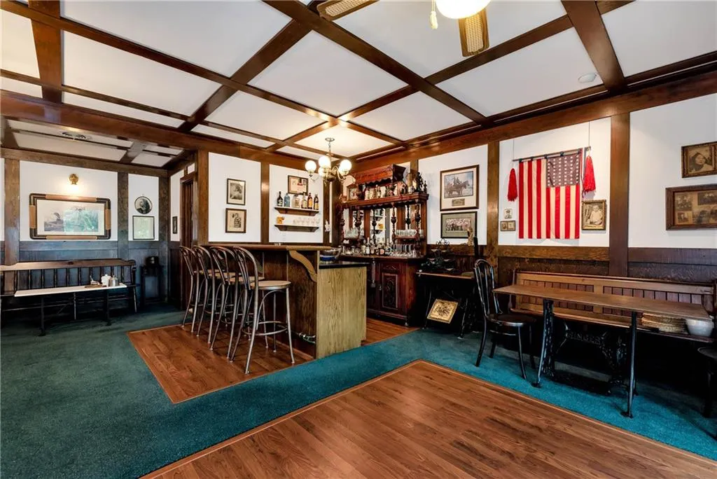 Bar with decorative light fixtures, dark wood-type flooring, coffered ceiling, and ceiling fan with notable chandelier