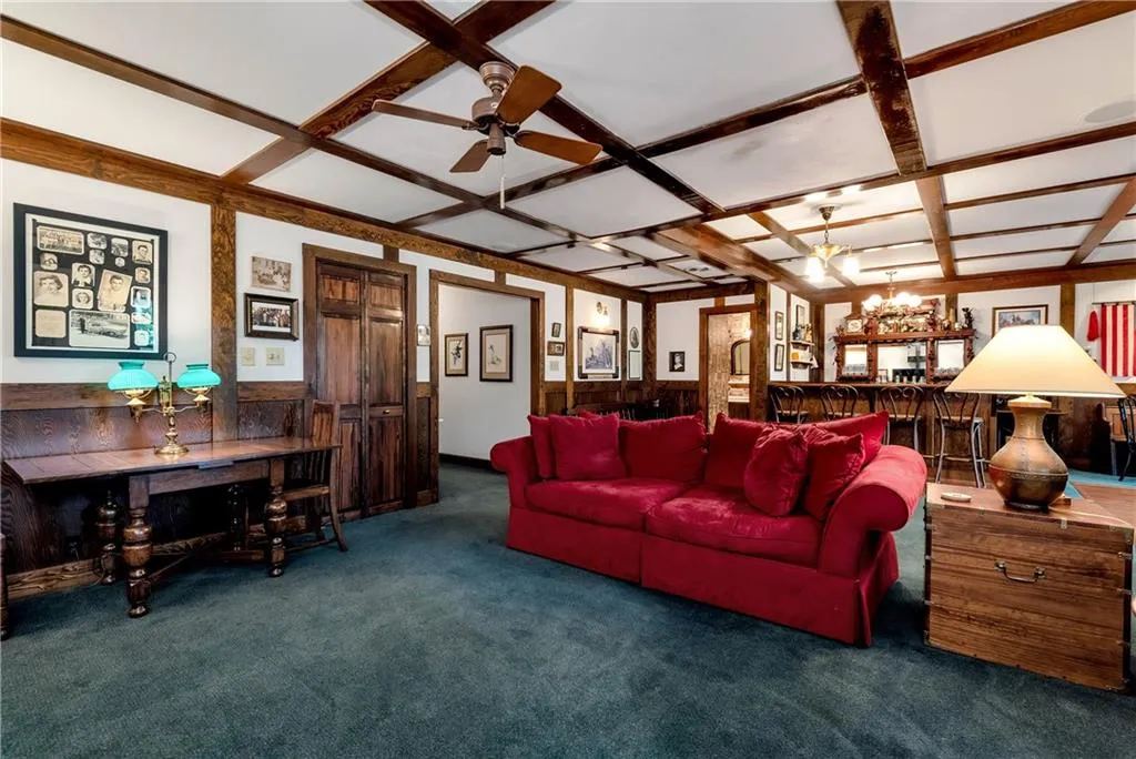 Living room featuring coffered ceiling, ceiling fan with notable chandelier, beamed ceiling, and dark carpet