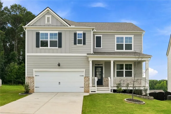 Two-story exterior featuring a covered front porch, a two-car garage, and a combination of shingle and siding materials