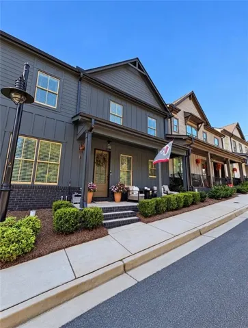 Modern townhome facade featuring dark siding, brick foundation, and a covered porch