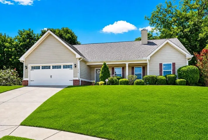 Ranch-style residence featuring a prominent front lawn, concrete driveway, attached garage with decorative windows, and a covered porch entry