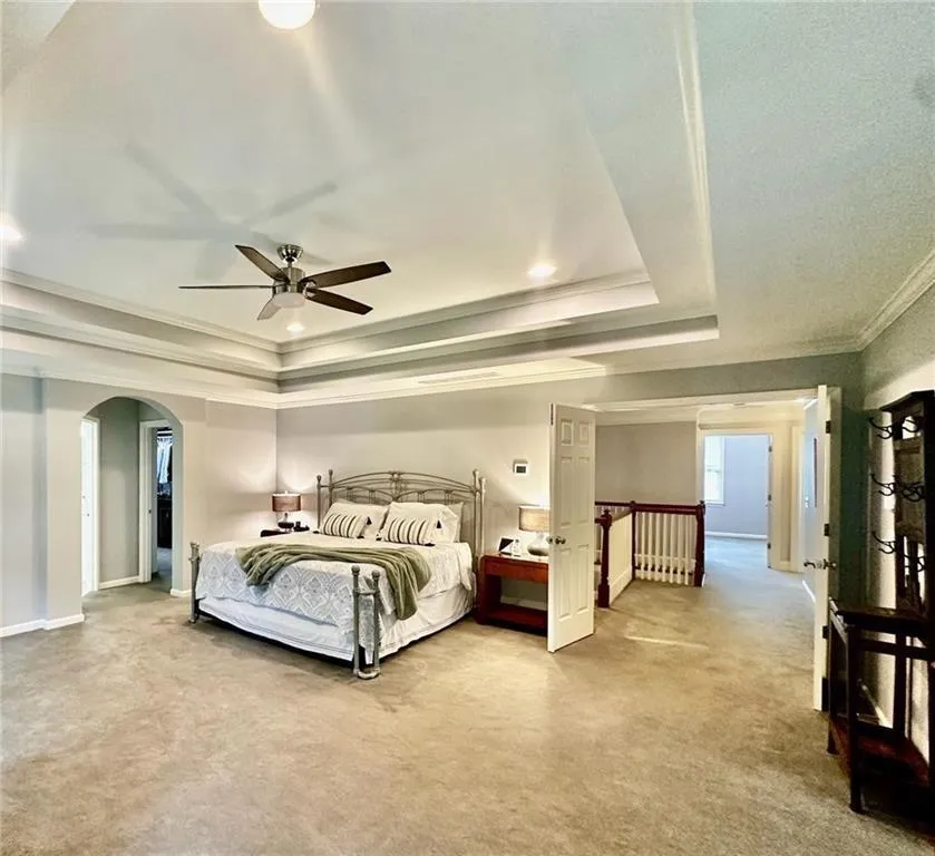 Bedroom featuring ceiling fan, a raised ceiling, carpet flooring, and crown molding