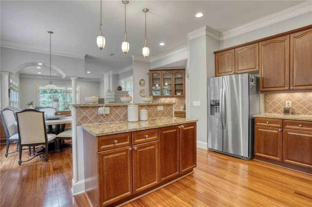 Kitchen with pendant lighting, crown molding, light hardwood / wood-style flooring, stainless steel refrigerator with ice dispenser, and decorative columns