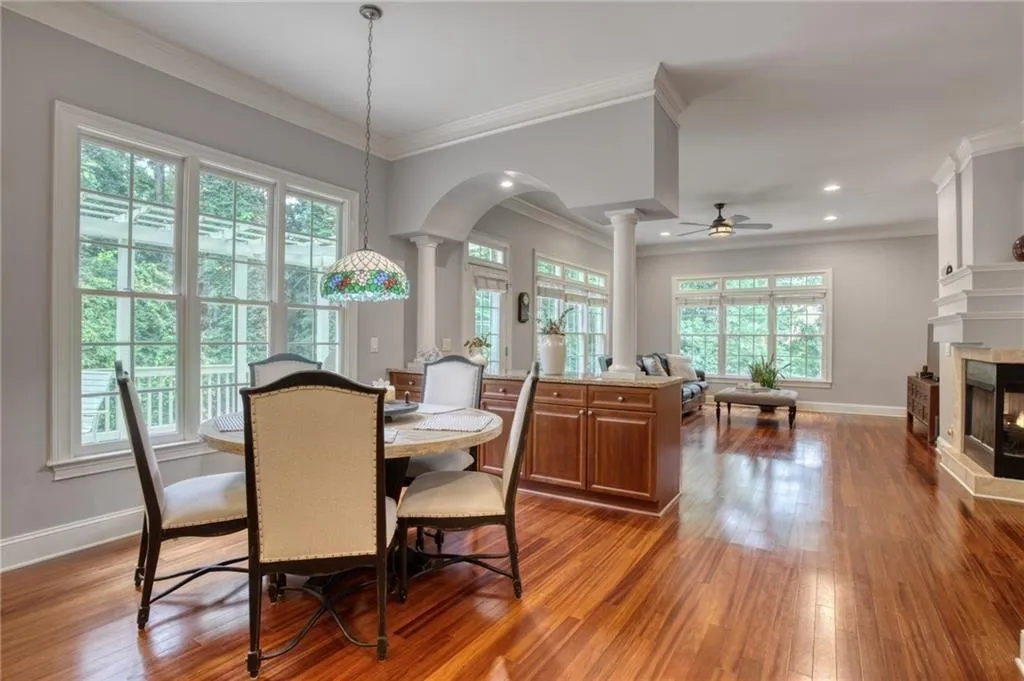 Dining space featuring light hardwood / wood-style floors, a multi sided fireplace, ornamental molding, ceiling fan, and ornate columns