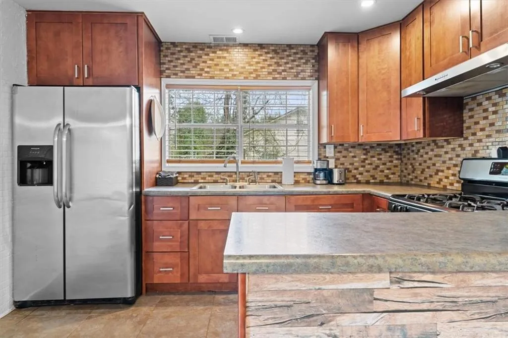 Kitchen featuring stainless steel appliances, backsplash, extractor fan, brown cabinetry, and recessed lighting