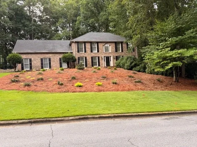 Traditional brick exterior featuring a dark shingle roof and black louvered shutters