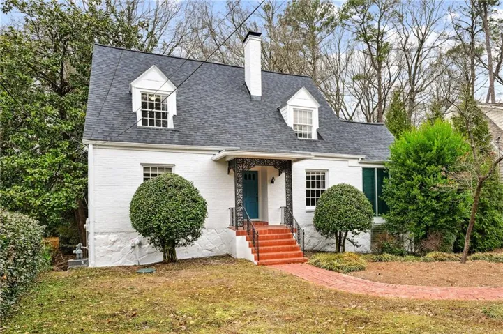 Cape cod house with a shingled roof, a chimney, brick siding, and a front yard