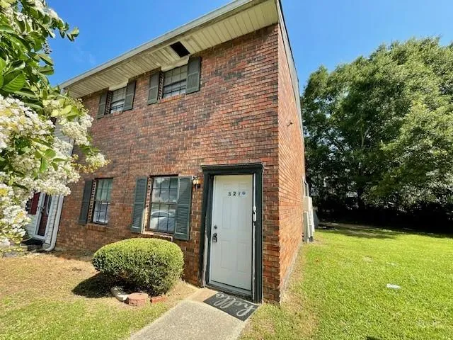 Brick facade townhouse featuring a white entry door, dark shutters, and a manicured shrub