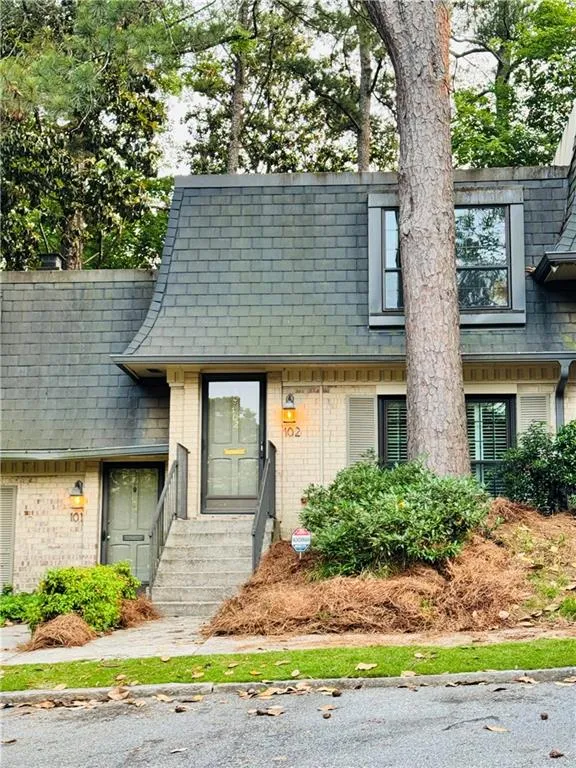 View of the townhome with its mansard roof, brick siding, and a composite slate shingled roof.