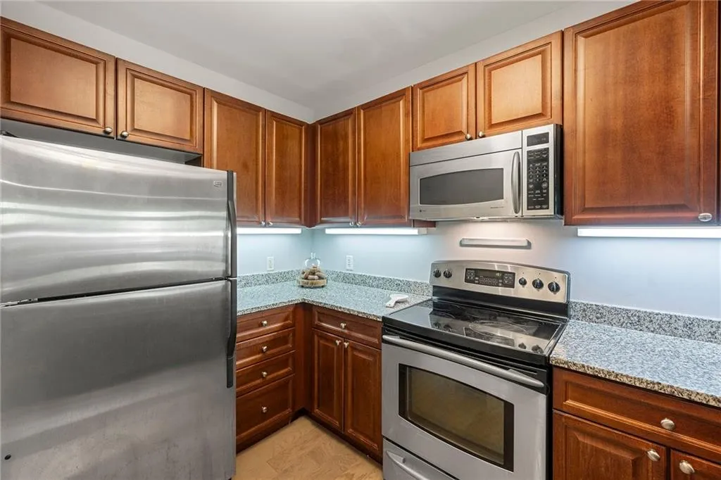 Kitchen with stainless steel appliances, light stone countertops, and brown cabinetry