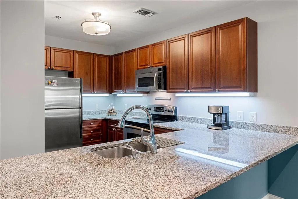 Kitchen featuring appliances with stainless steel finishes, light stone counters, a peninsula, and brown cabinets