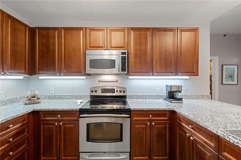Kitchen featuring stainless steel appliances, light stone counters, and brown cabinets