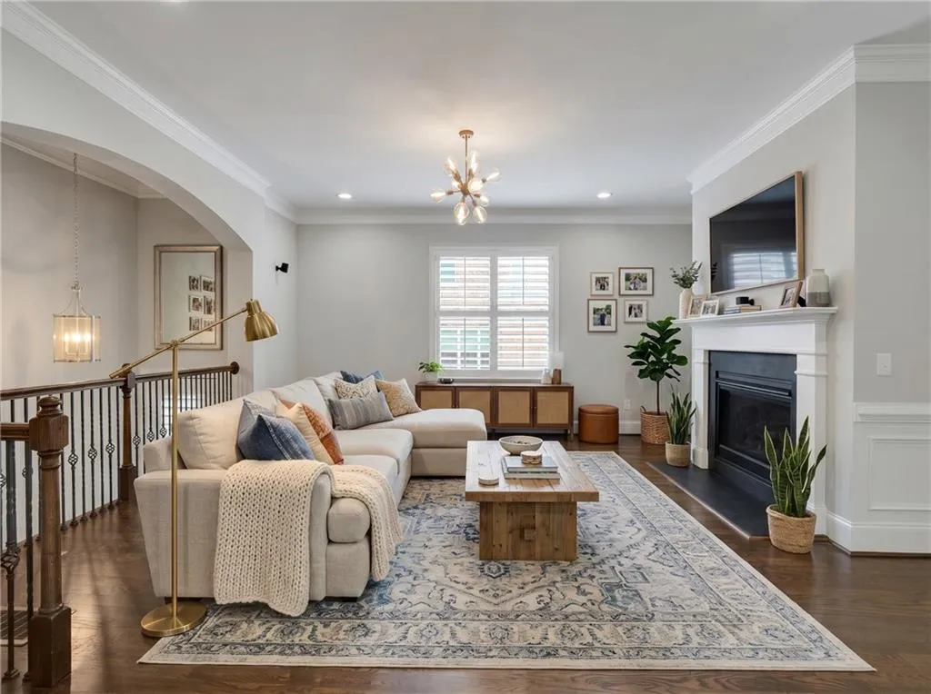 Spacious living area featuring wood-finish flooring, a fireplace with a white mantel, and crown molding