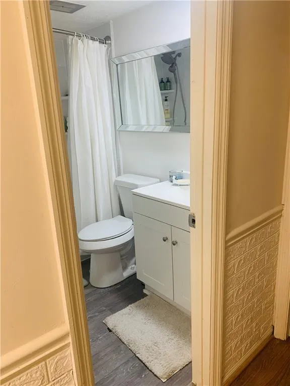 Bathroom featuring vanity, dark wood-type flooring, curtained shower, and wainscoting