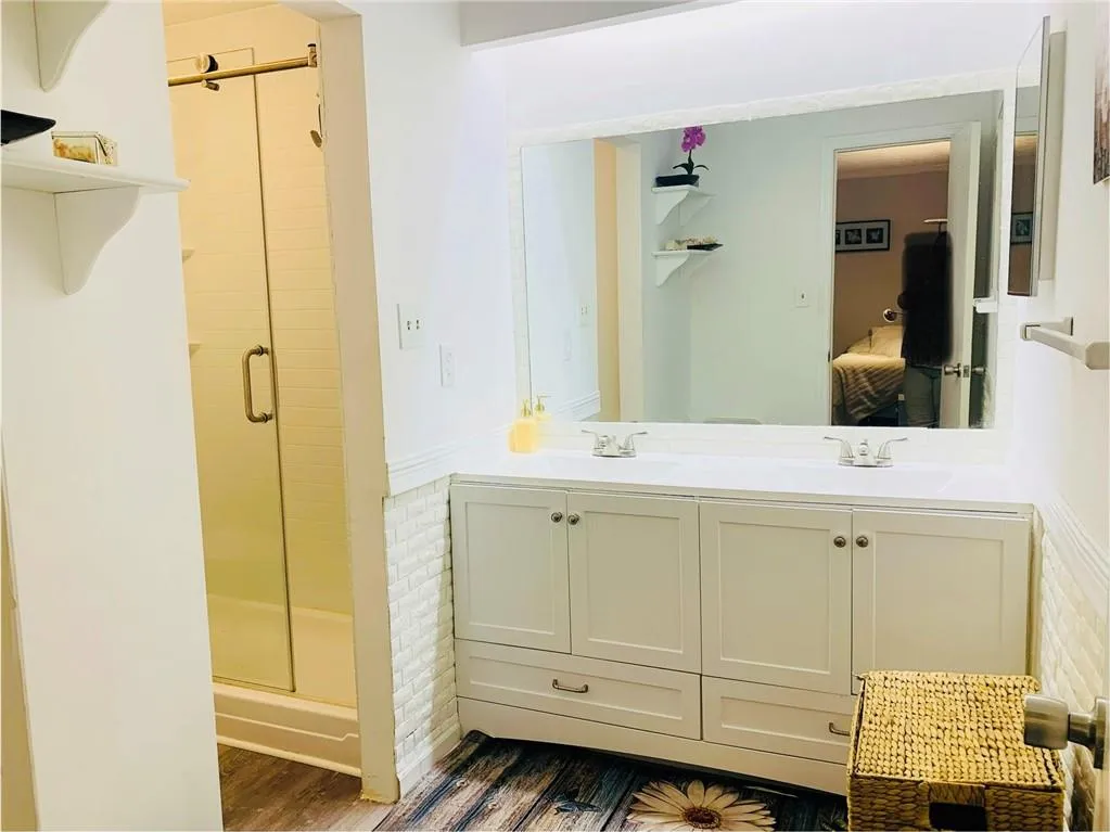 Ensuite bathroom with double vanity, dark wood-style floors, and a shower stall
