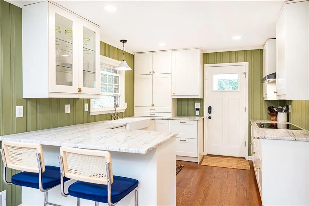 Kitchen with white cabinetry, a peninsula, a kitchen breakfast bar, glass fronted cabinets, and wooden walls