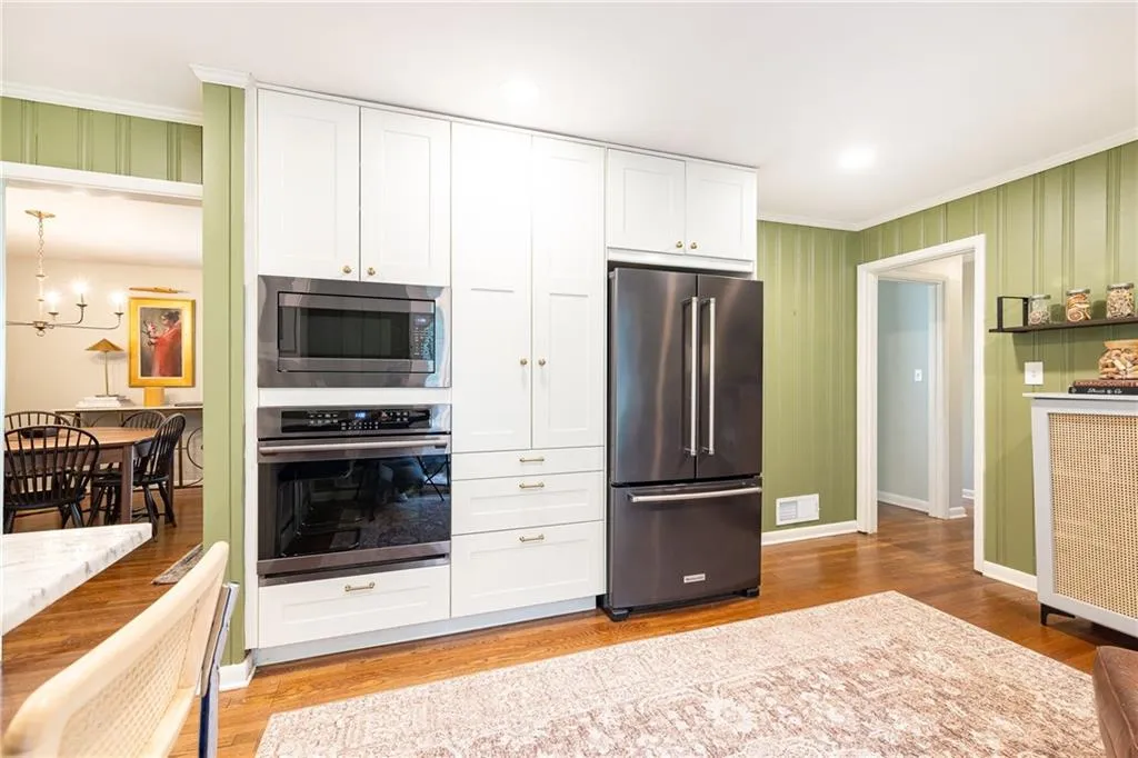 Kitchen with stainless steel appliances, white cabinetry, light wood-style floors, crown molding, and wallpapered walls