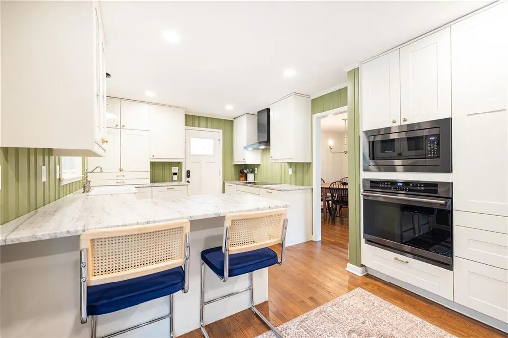 Kitchen featuring a kitchen breakfast bar, stainless steel appliances, light stone countertops, white cabinets, and light wood-style floors