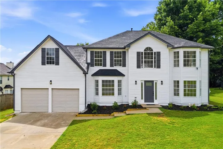 Two-story white siding residence featuring a two-car garage, dark gray front door, multiple bay windows, and black exterior shutters