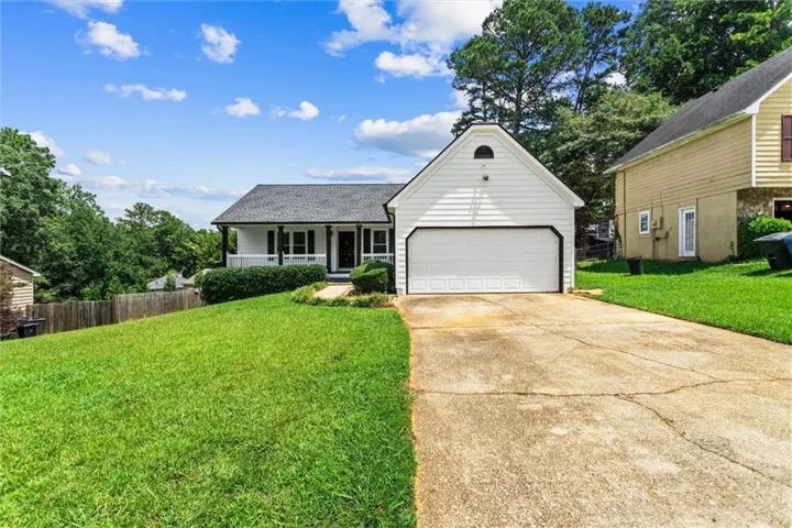 White siding exterior with a prominent two-car garage, front porch, and a sloped lawn