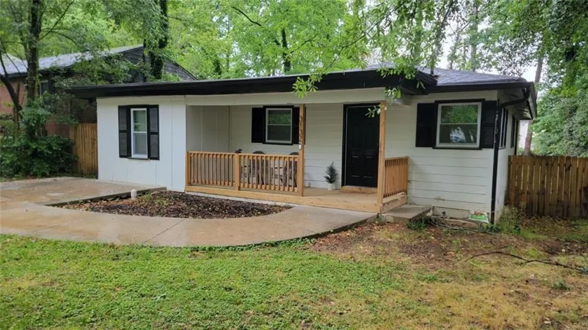 White exterior siding with black shutters, a wood-finish porch, and a dark asphalt shingle roof