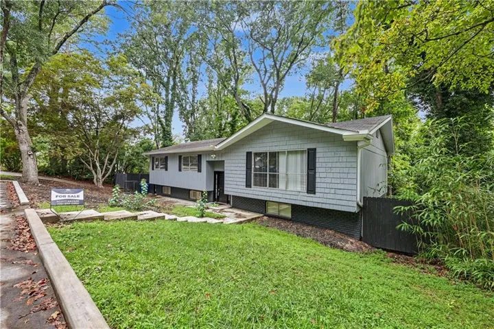 Light gray siding with dark shutters, front yard with mature trees, established landscaping with stone path, and a black privacy fence