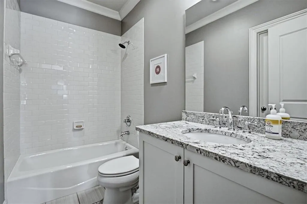 Subway tile shower surround, integrated bathtub, vanity with stone countertop, undermount sink, and chrome fixtures