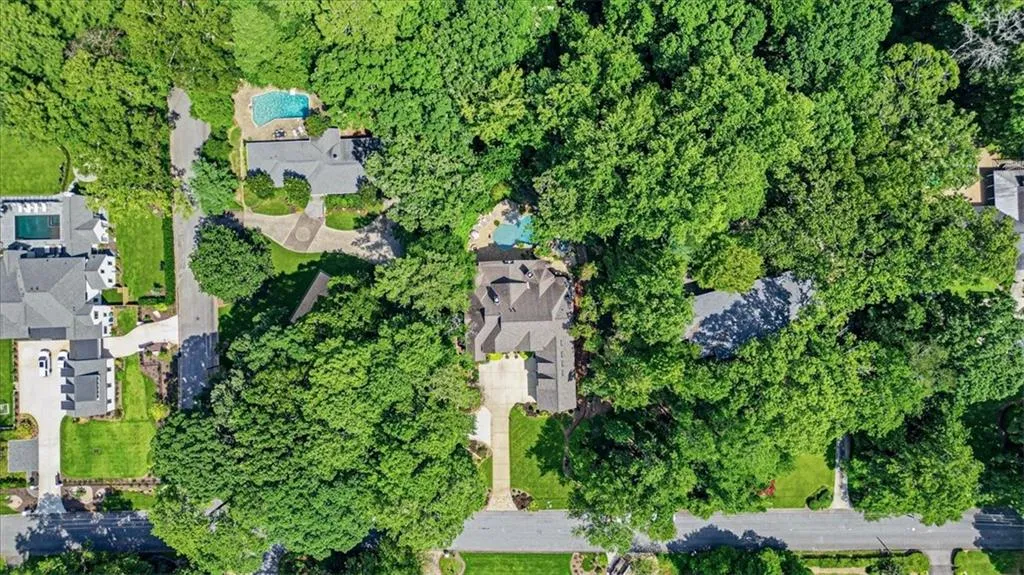Aerial perspective showcasing a residential property with a multi-level roofline, extensive mature tree coverage, and a paved driveway