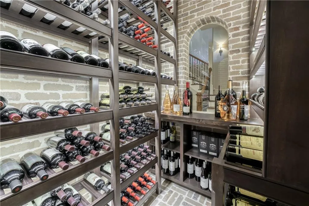 Brick-lined wine cellar featuring extensive dark wood shelving, a built-in counter surface, and an arched brick entryway