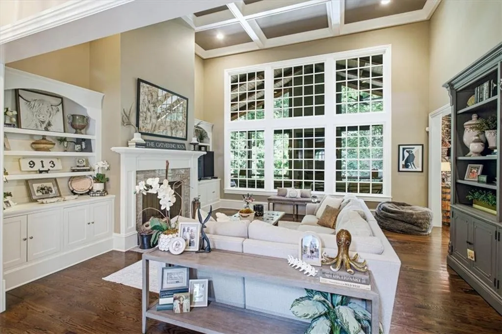 Soaring coffered ceilings, expansive grid-pattern windows, built-in cabinetry, elegant fireplace with mantel, and wood-finish flooring