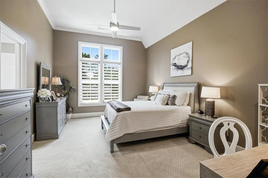 Tray ceiling with crown molding, ceiling fan, carpeted flooring, window with plantation shutters, and a framed doorway